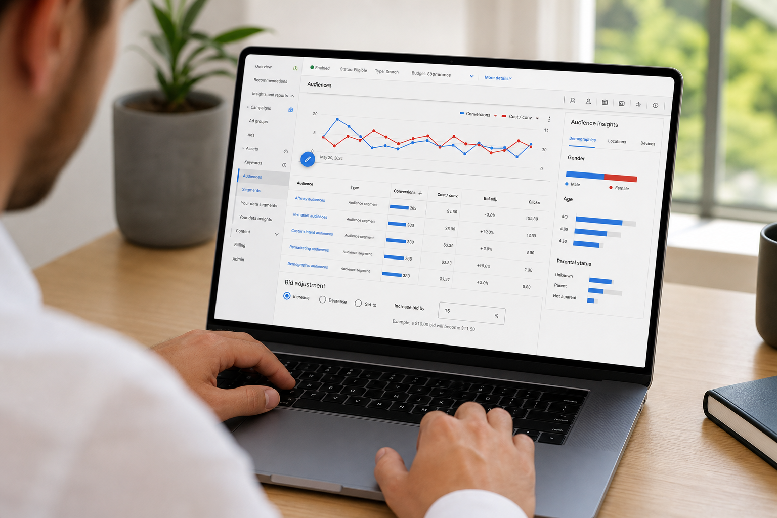 Close-up of a Google Ads Manager campaign dashboard showing audience segment performance metrics, bid adjustments, and conversion data on a laptop screen in a bright workspace