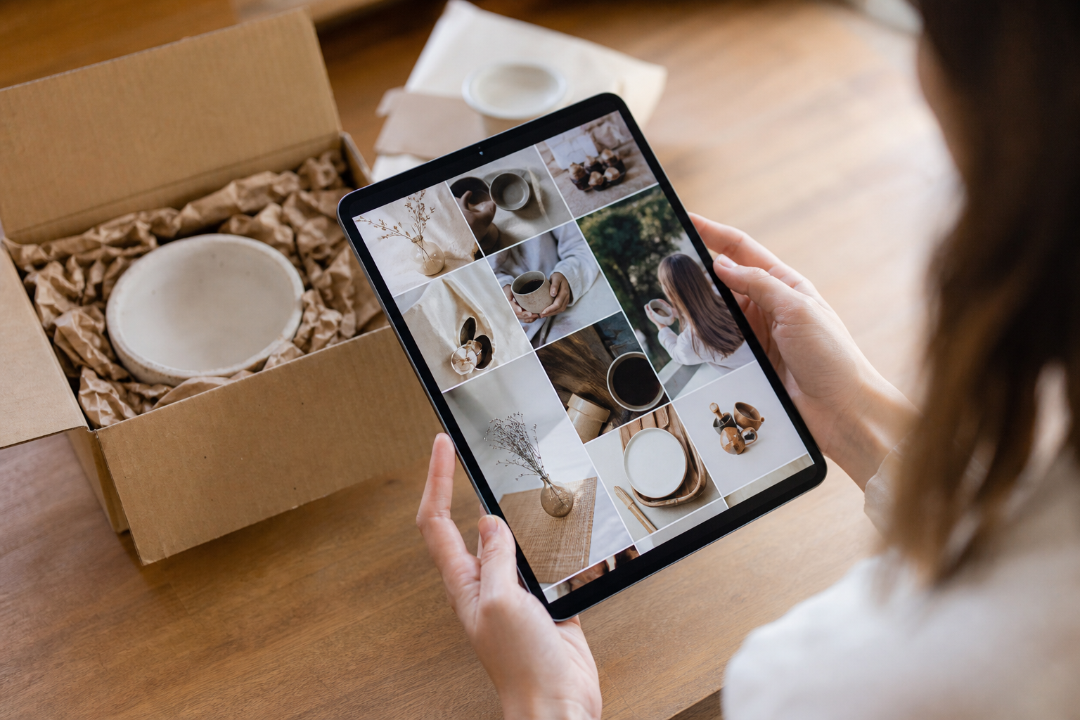 A Shopify ecommerce brand's social media feed displayed on a tablet, showing product lifestyle images in warm natural lighting on a wooden desk with packaging props nearby